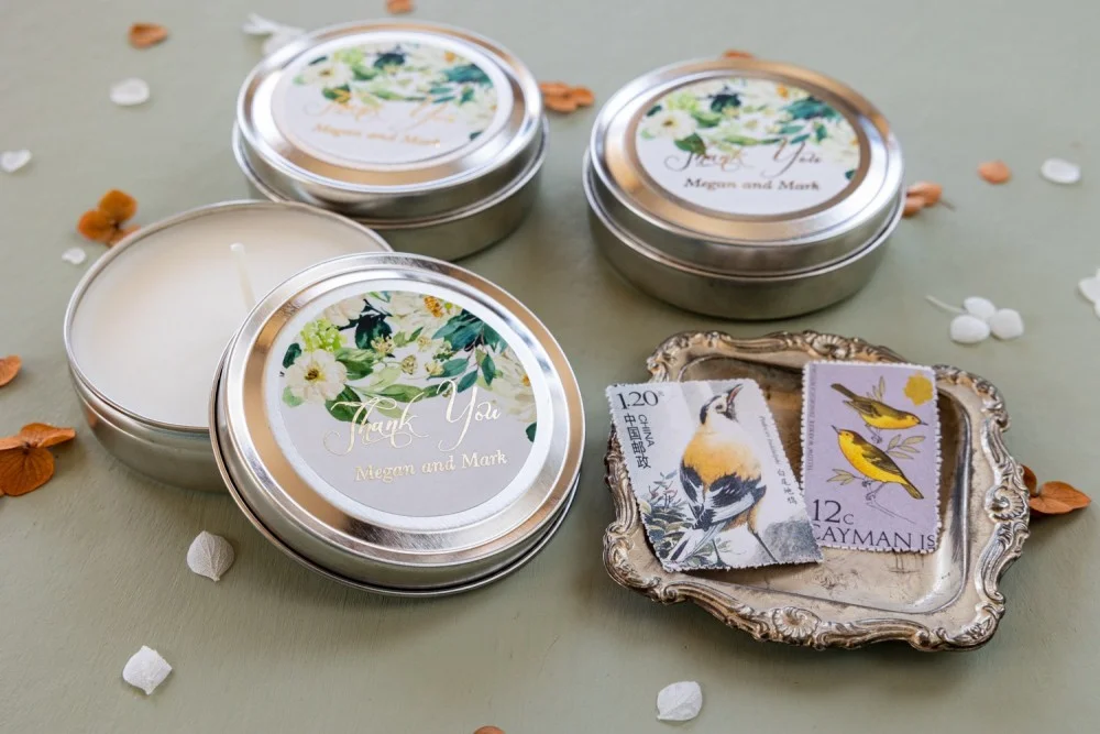 Velas de cera de soja personalizadas y hechas a mano para los invitados de su boda con texto dorado y flores blancas.