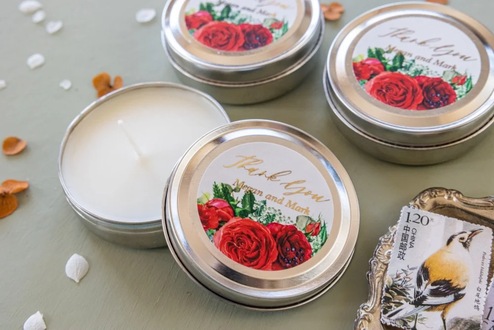 Bougies de cire de soja faites à la main, pour les invités d'un mariage, avec un texte en or et des fleurs de rose rouges.