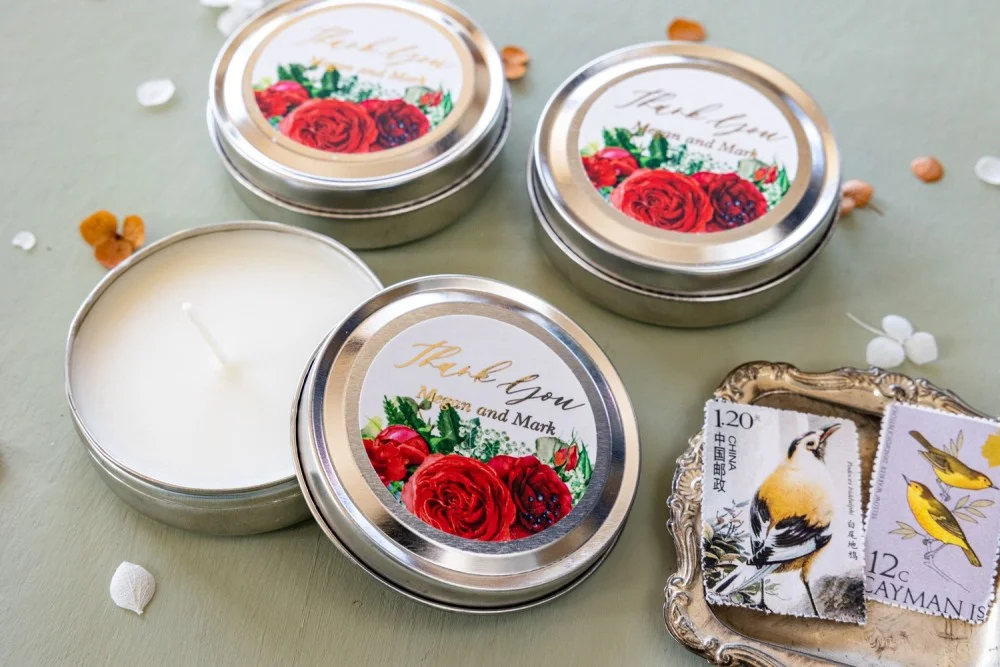 Bougies de cire de soja faites à la main, pour les invités d'un mariage, avec un texte en or et des fleurs de rose rouges.