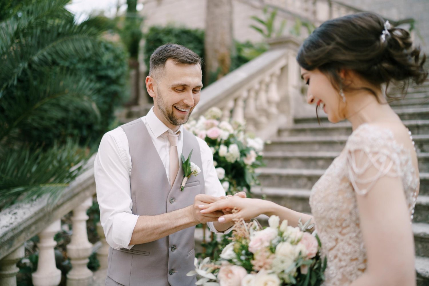 Smiling groom puts the ring on the bride finger while standing on the steps