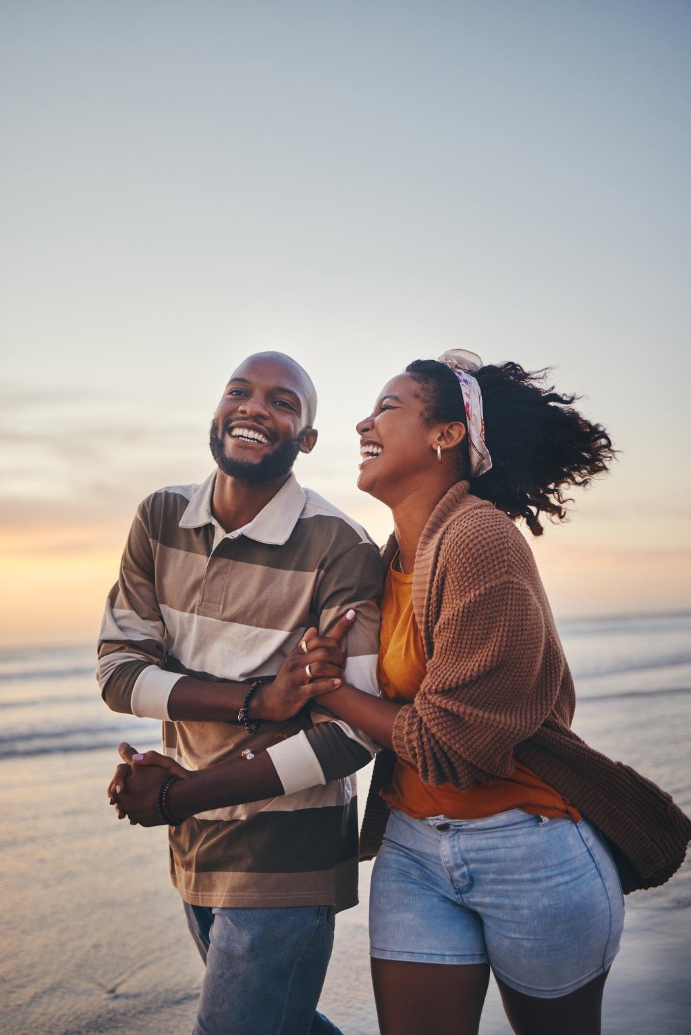 Happy couple love and travel at the beach holding hands on date quality time and romance at sunset Black woman and man laughing and walking together by the ocean on honeymoon during summer