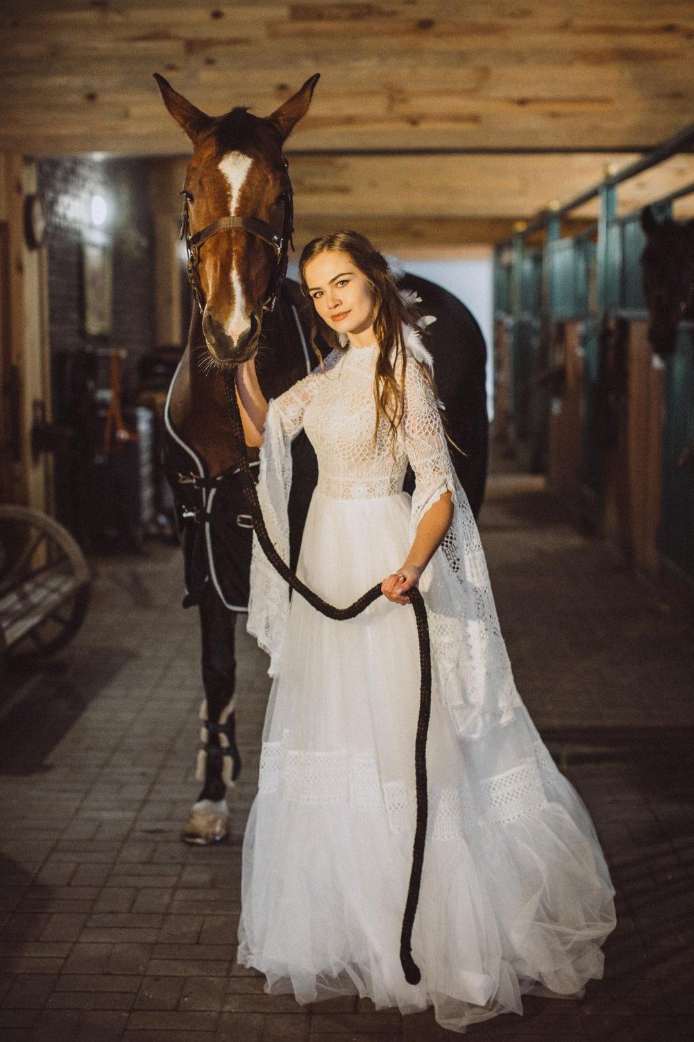 boho bride poses with a horse in a stable