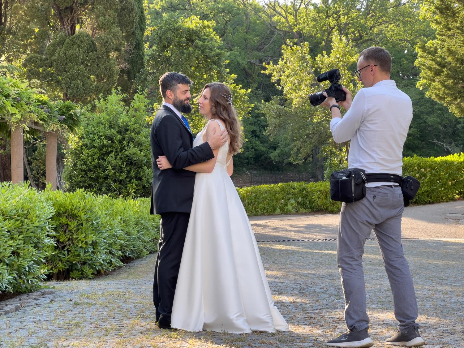 male photographer photographing bride and groom standing in the garden
