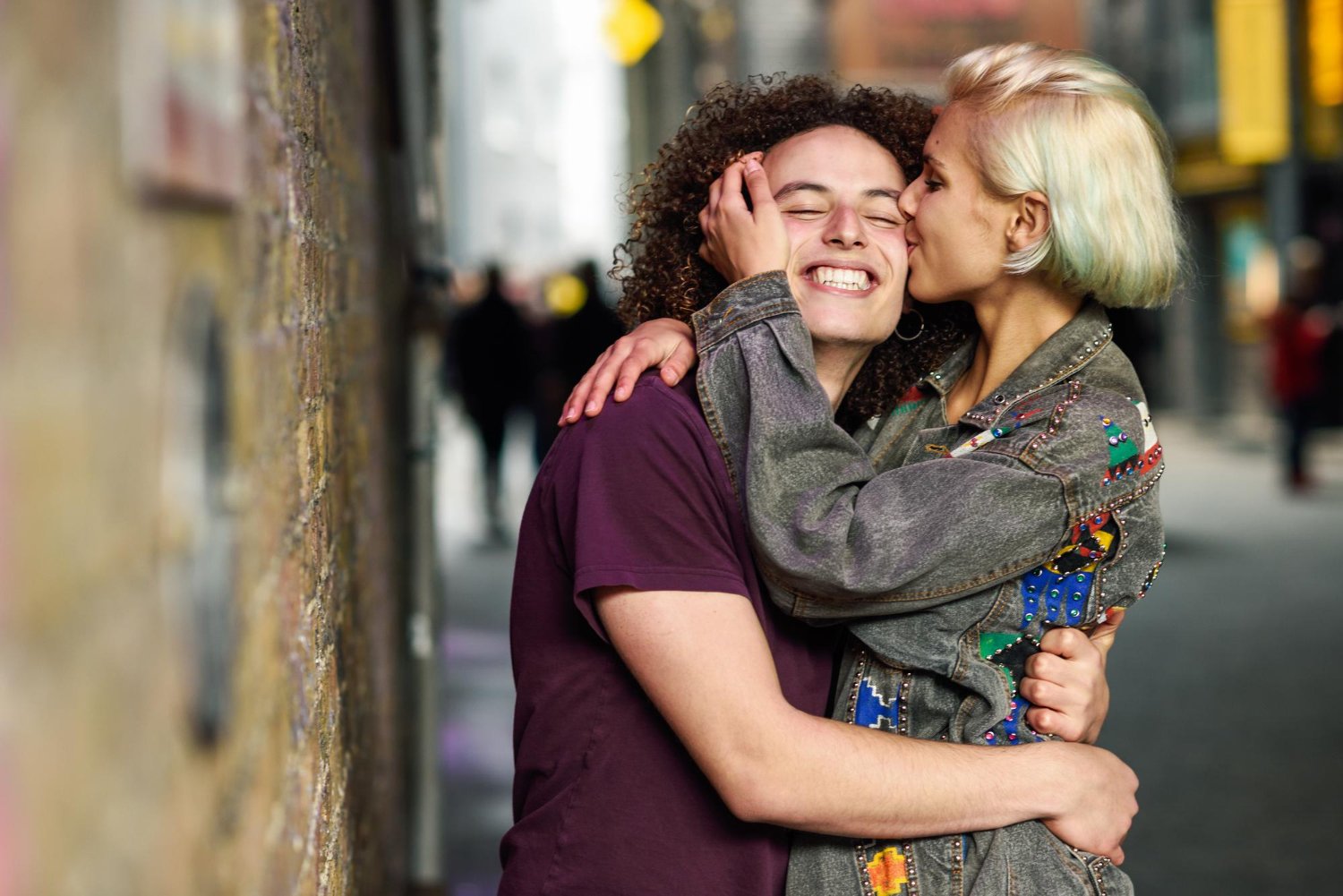 Photo smiling young woman kissing friend on footpath in city