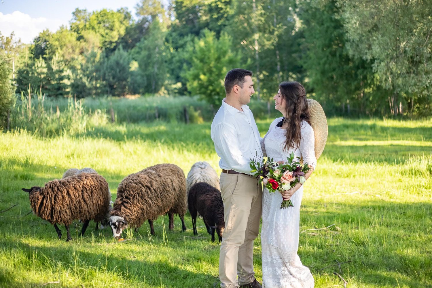 young beautiful couple in love in wedding dresses standing on a green meadow cattle in the background